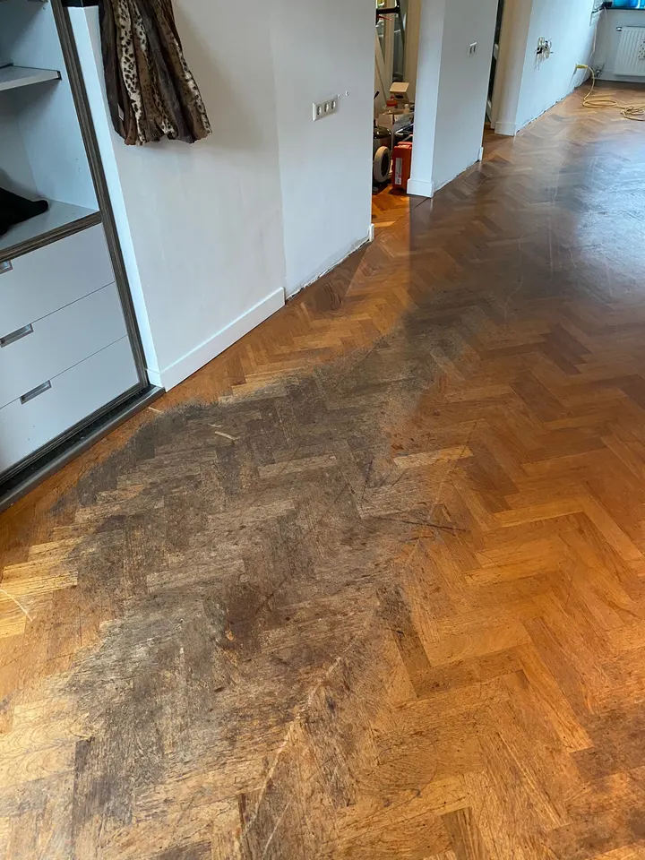 Eiken visgraatparket in een hal, donker verkleurd door waterschade voor een kledingkast